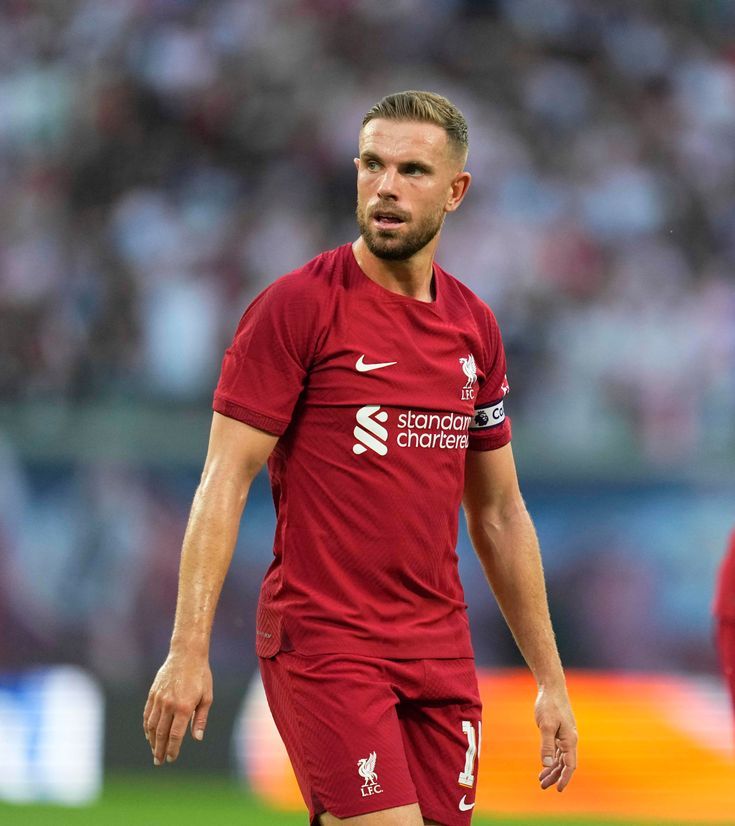 a soccer player in red is on the field during a game and looks to his left