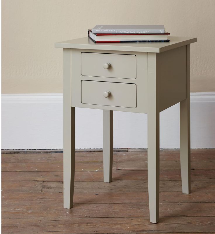 a small white table with two drawers and a stack of books sitting on top of it