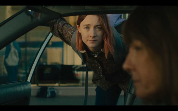 a woman with red hair sitting in the driver's seat of a car looking at another woman