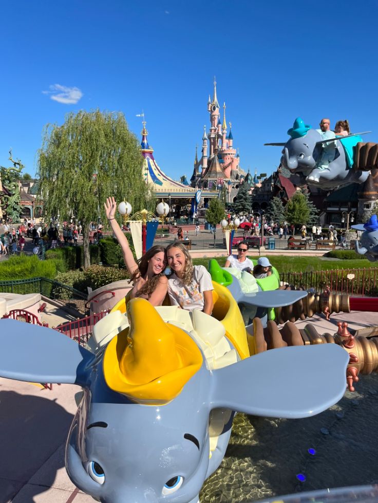 two girls are riding in an elephant ride at the amusement park while others look on