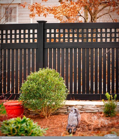 an owl statue in front of a black fence and shrubbery with autumn leaves around it