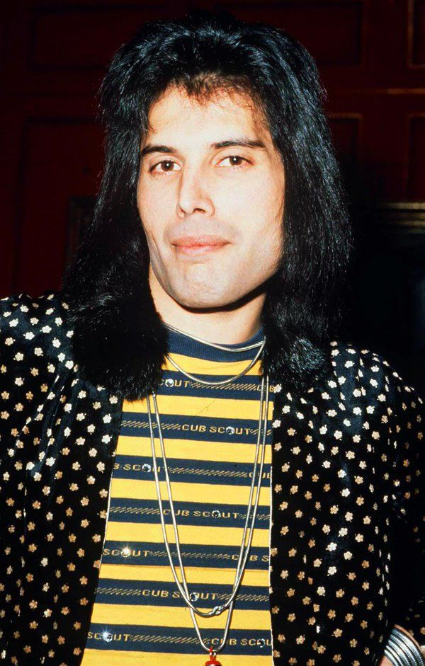 a man with long black hair wearing a yellow and black striped shirt is looking at the camera