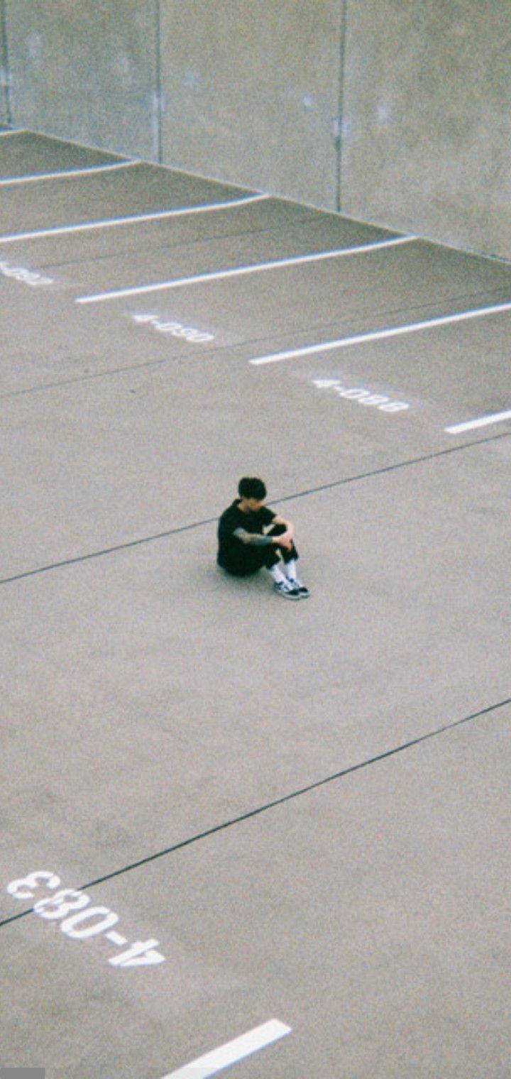 a person sitting on the ground in an empty parking lot