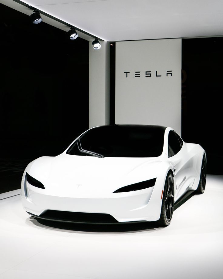 a white tesla car is parked in front of a black and white wall with the word tesla on it