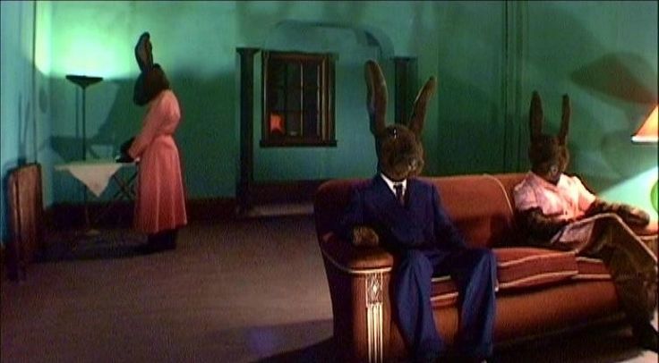 two rabbits sitting on top of a couch next to a man in a suit and tie