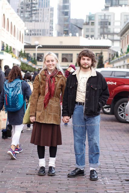 a man and woman standing next to each other on a brick sidewalk in front of tall buildings