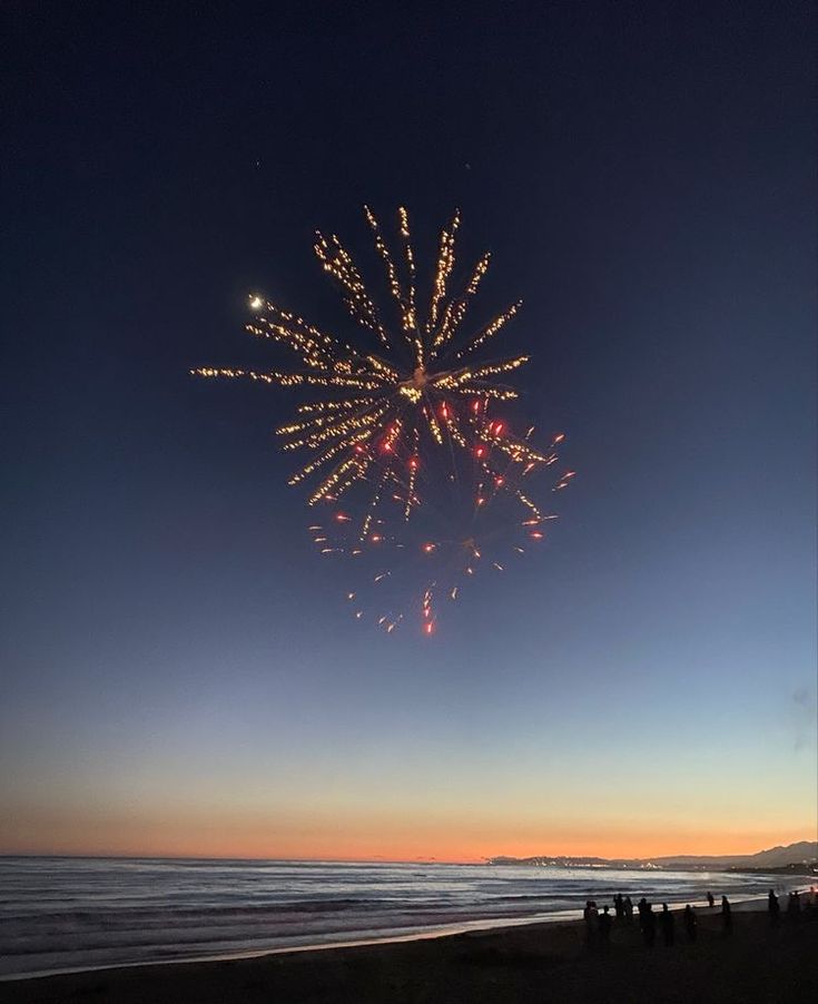 people are standing on the beach watching fireworks