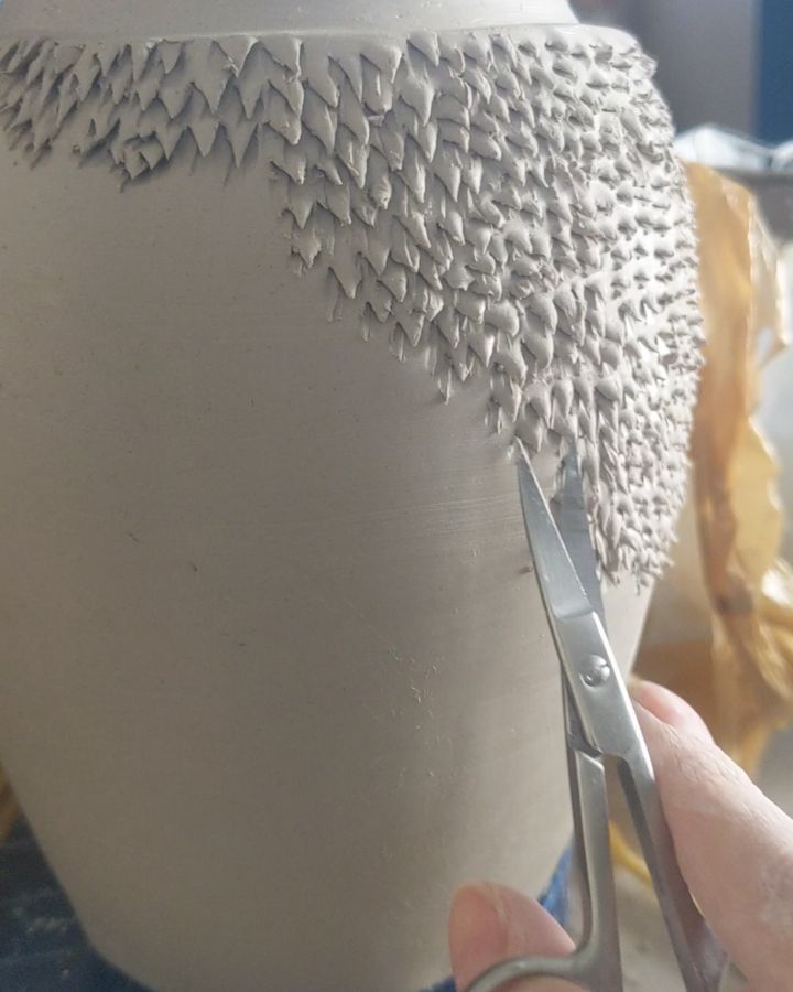 a person is cutting through the bottom of a white vase with scissors in front of it