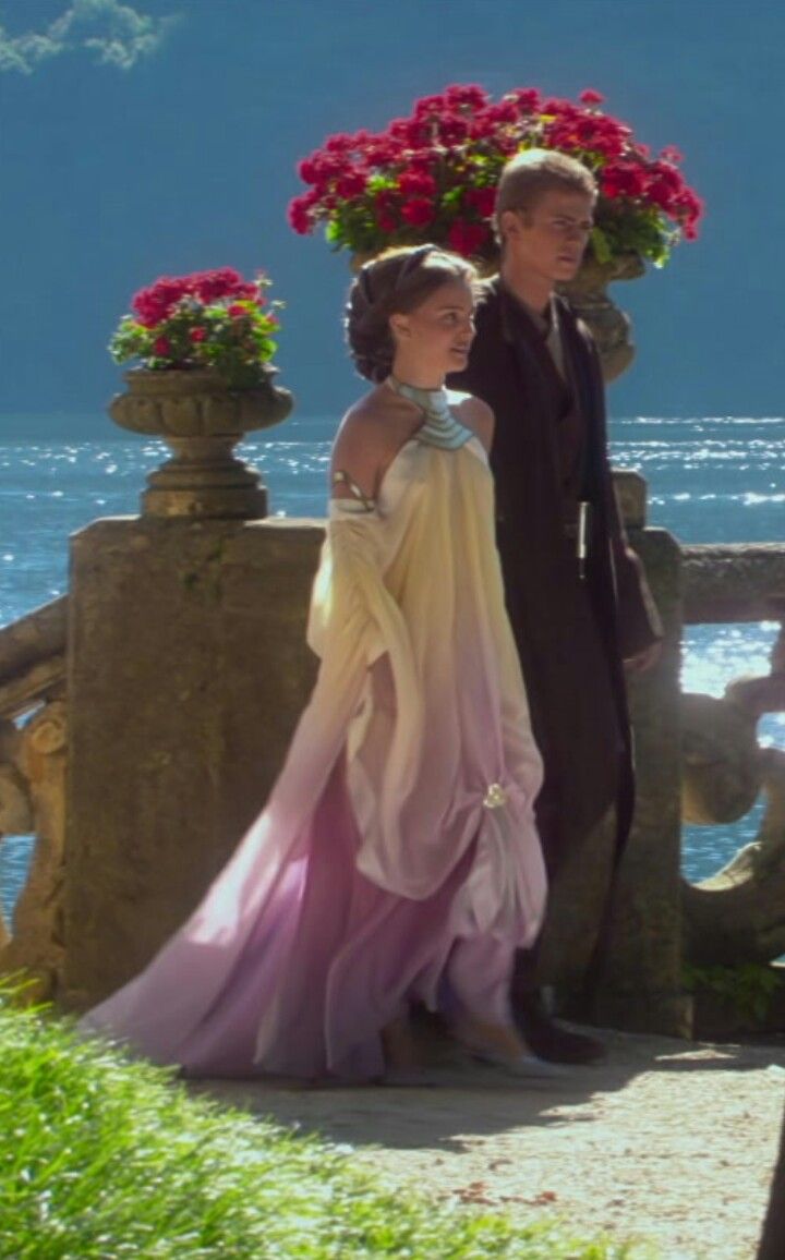 a man and woman dressed in formal wear walking on a path next to the ocean