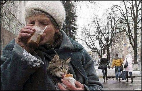 a woman drinking from a bottle while holding a cat in her lap on the street