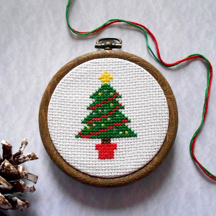 a cross stitch christmas ornament with a pine tree on it next to some cones