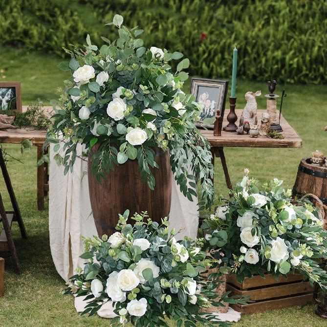 an arrangement of white flowers and greenery on display in front of a wooden barrel