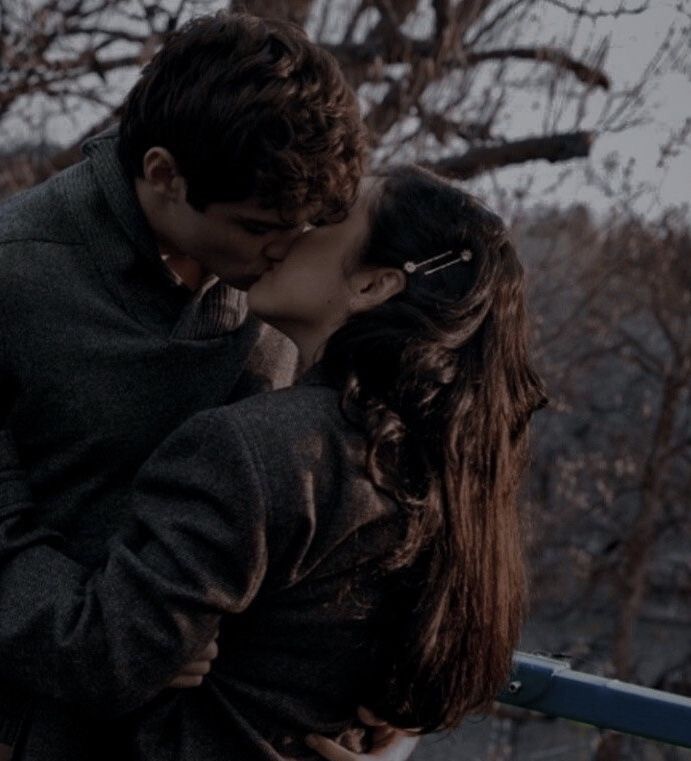 a man and woman kissing in front of trees