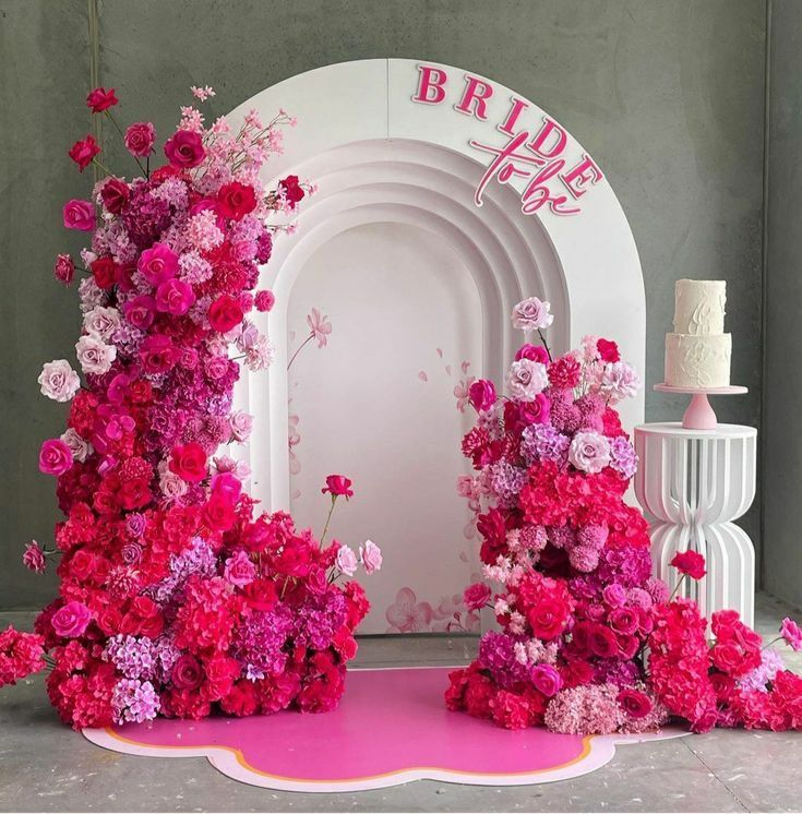 pink and white flowers are arranged in front of a arch