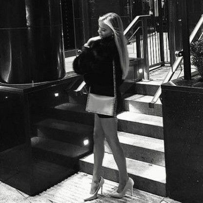 black and white photograph of woman in short skirt standing on steps with handbag near railing