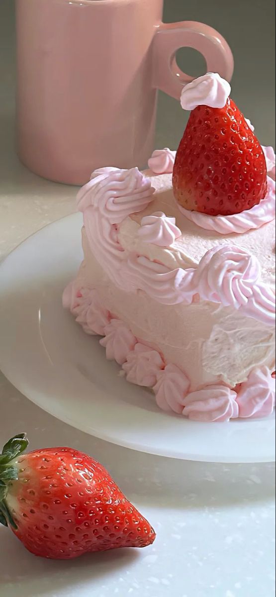 a strawberry sitting on top of a white plate next to a pink cup and saucer