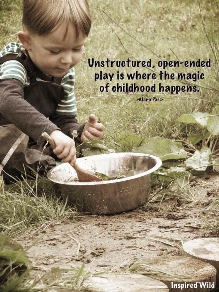 a little boy sitting in the grass playing with a metal bowl and spoon on top of it