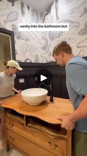 a man and woman standing in front of a wooden table with a bowl on it