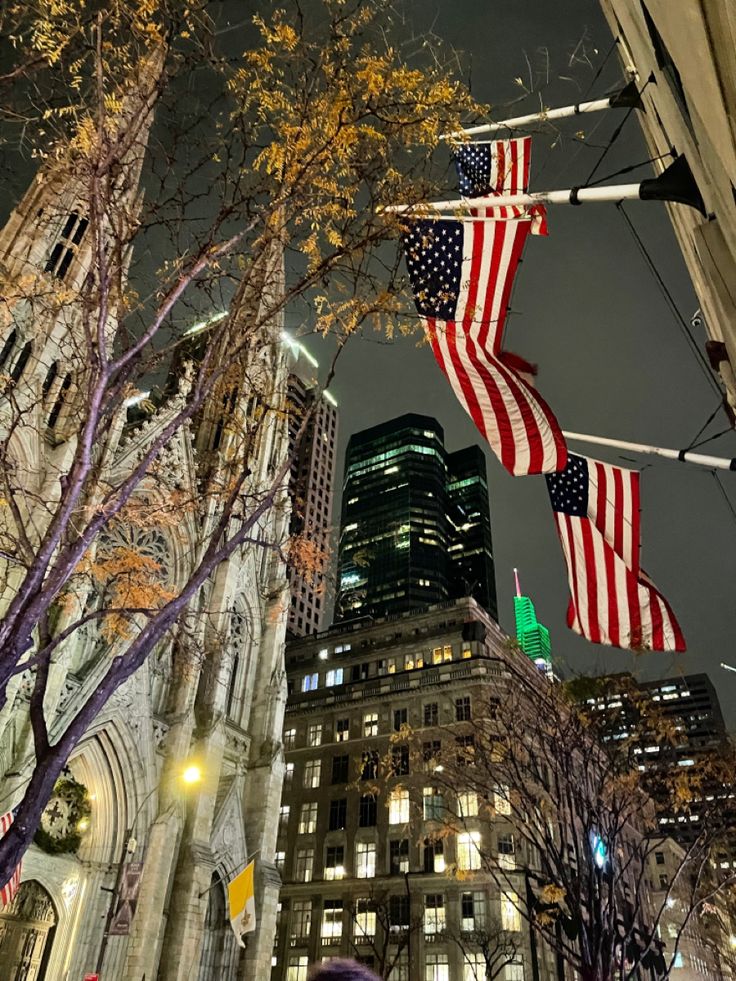 an american flag hanging from the side of a tall building in a city at night