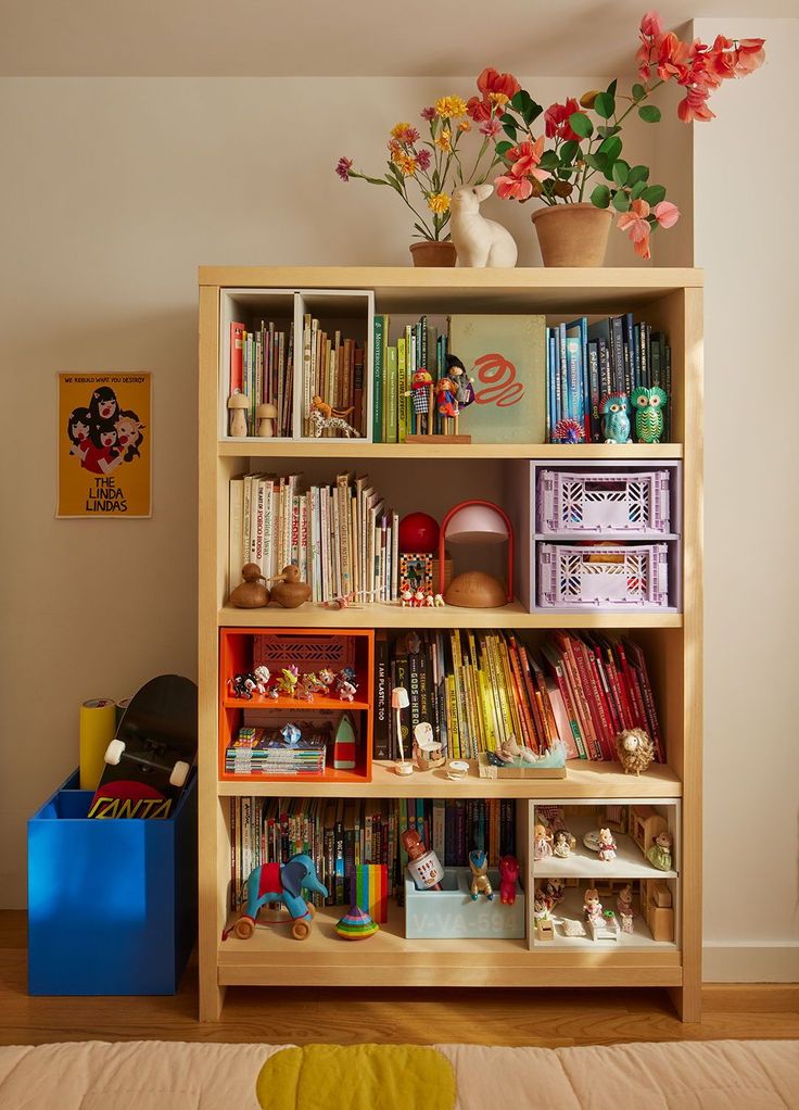 a bookshelf filled with lots of books next to a blue box and flowers