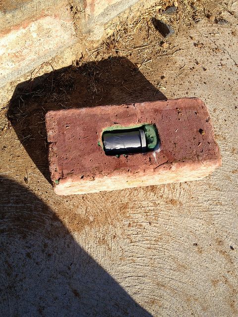 a cell phone laying on top of a piece of red brick next to a wall