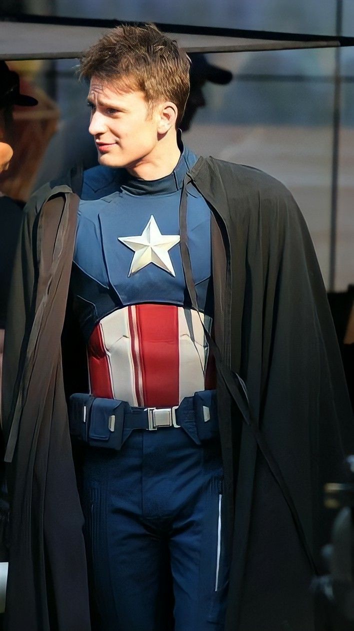 a man dressed up as captain america standing in front of a building with his cape open