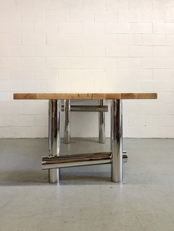 a wooden table sitting on top of a metal stand in front of a white brick wall