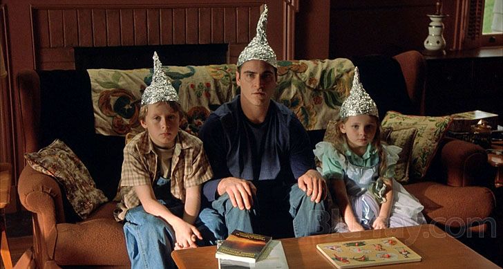 three children wearing party hats sitting on a couch with an adult in the back ground