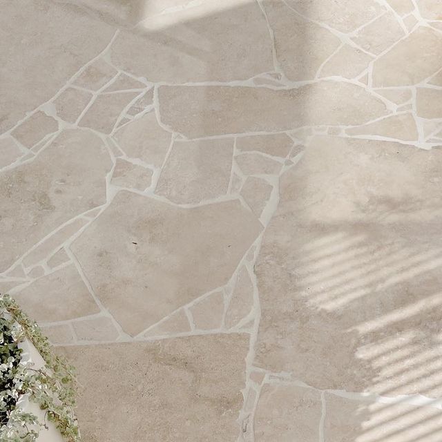 a white bench sitting on top of a stone floor next to a planter filled with flowers