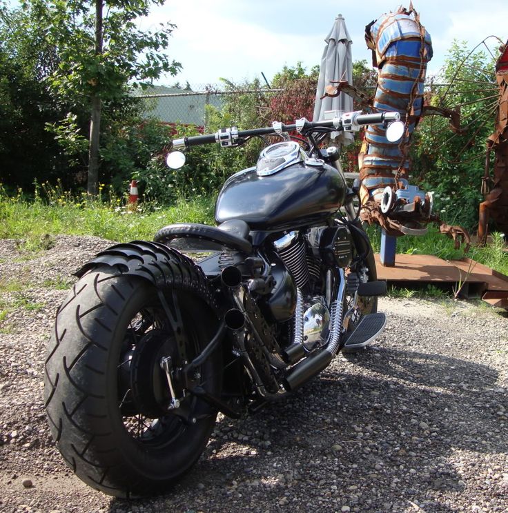 a black motorcycle parked on top of a gravel road next to a wooden structure and trees