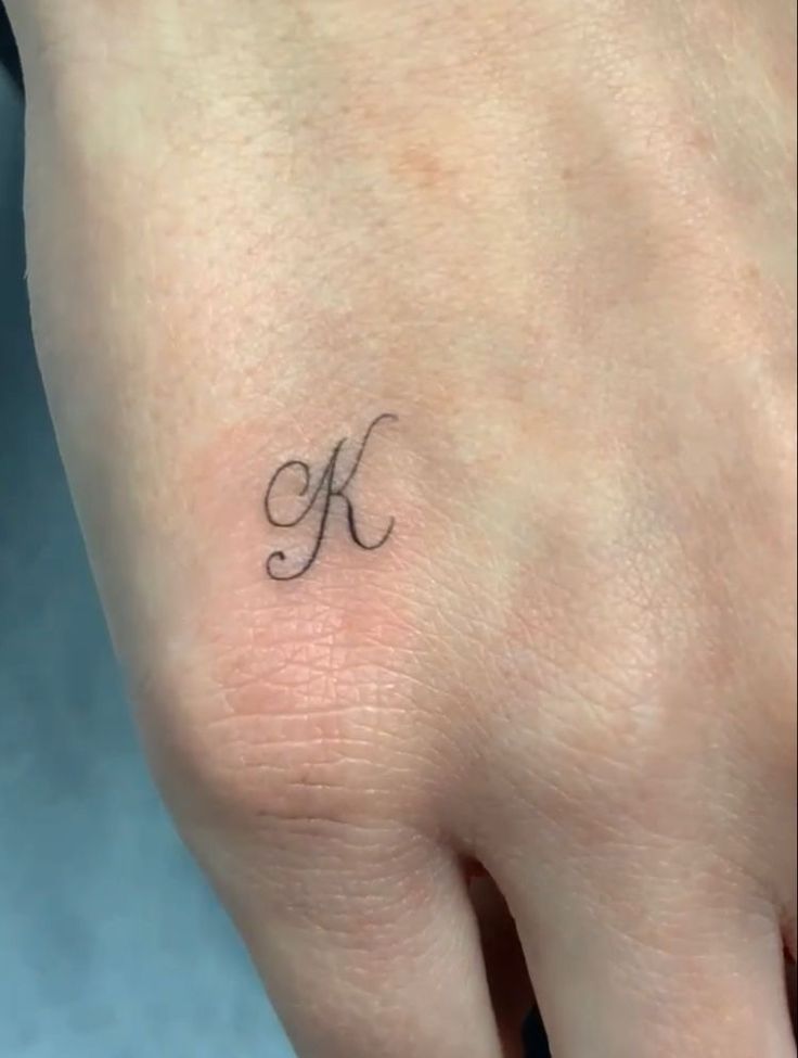 a small letter k tattoo on the left side of her hand is shown in black ink