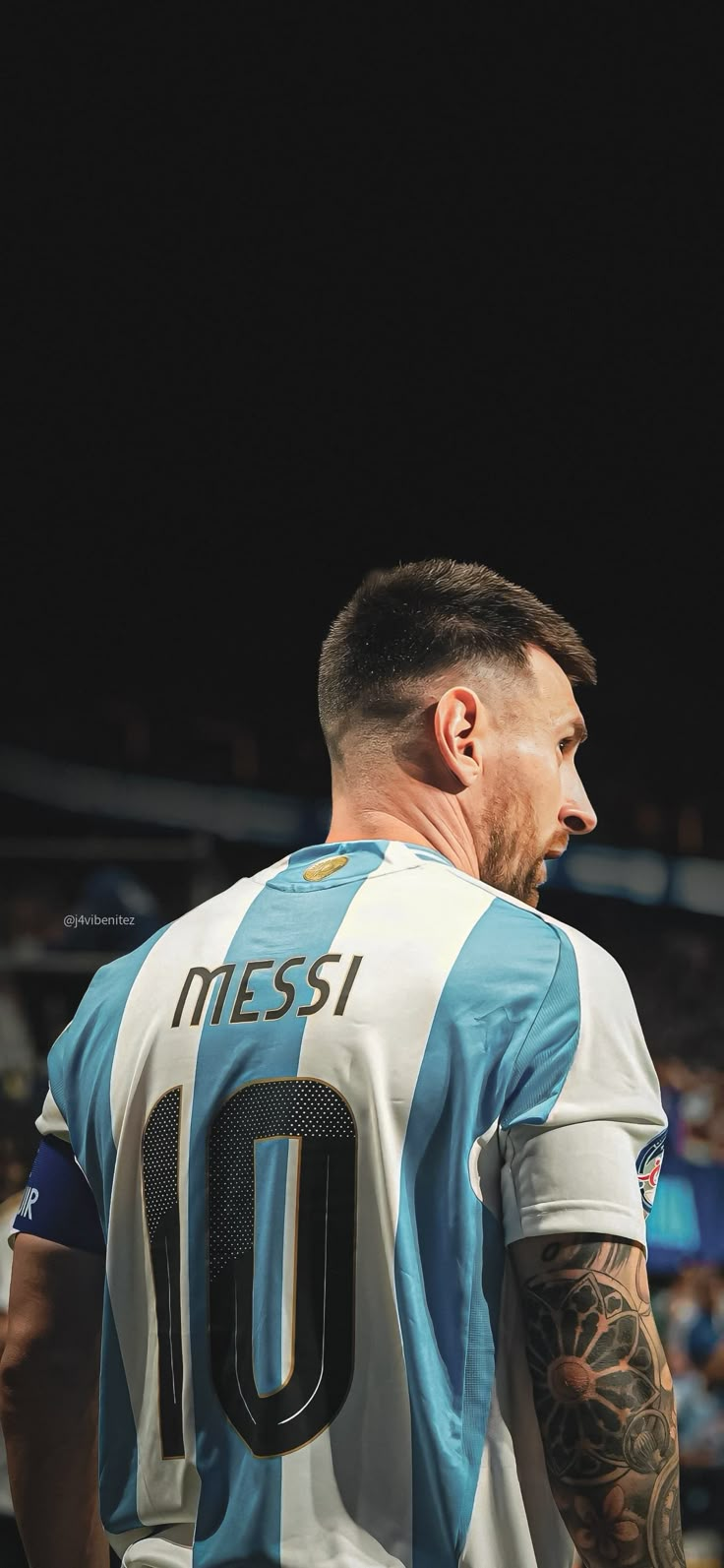 a man with tattoos on his arm standing in front of a crowd wearing a blue and white shirt