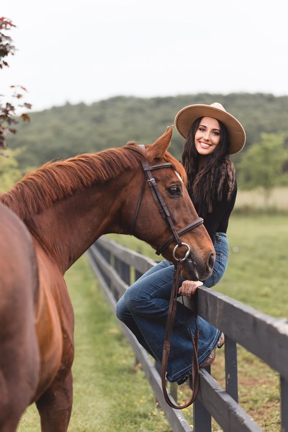 a woman wearing a cowboy hat leaning on a fence next to a horse