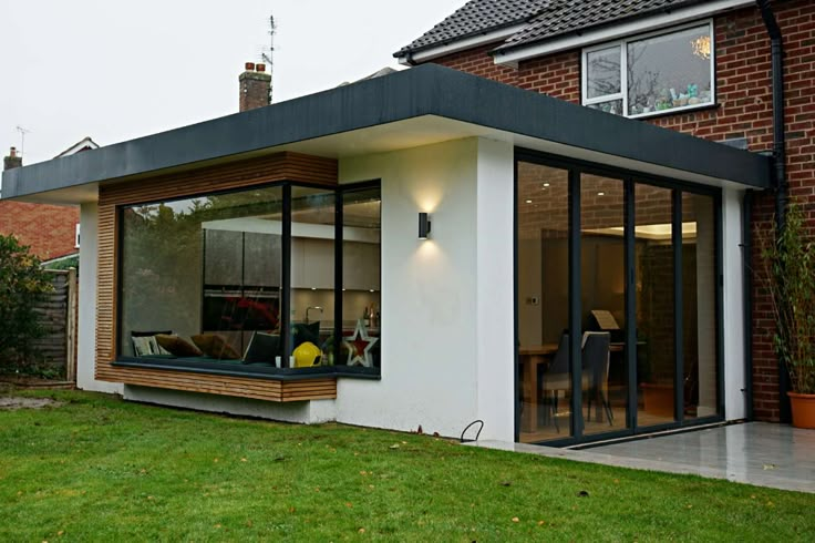 a modern house with large windows and sliding glass doors on the outside, in front of a brick building