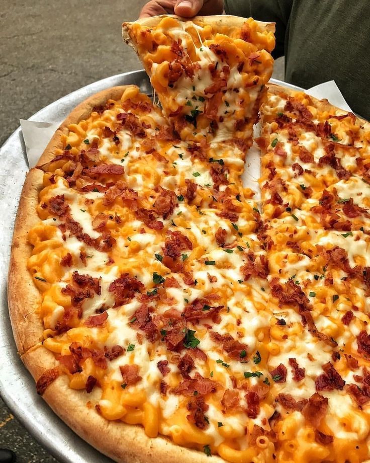 a person holding a slice of pizza with cheese and bacon on it