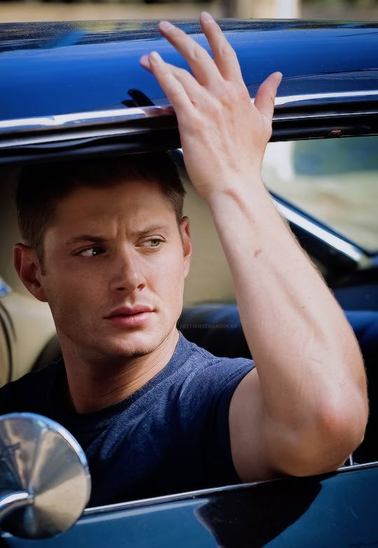 a man sitting in the driver's seat of a blue car with his hand on the door handle