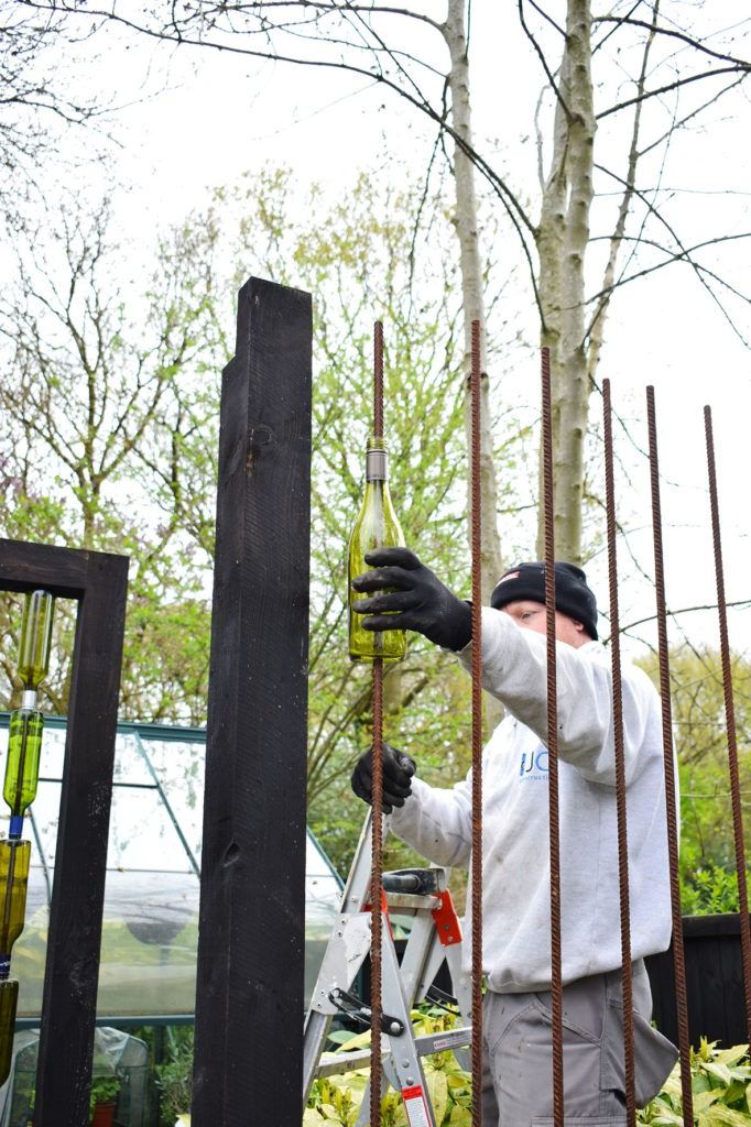 a man in white shirt and black gloves working on a fence with trees behind him