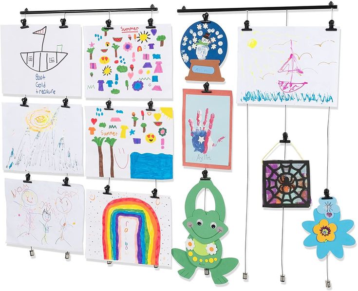 a group of children's artwork hanging from hooks on a white wall next to each other