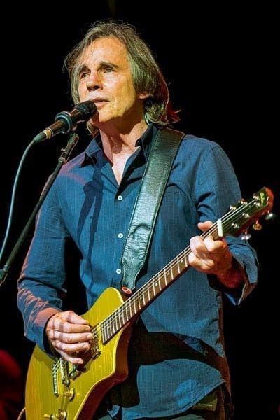 a man holding a yellow guitar while standing next to a microphone on top of a stage