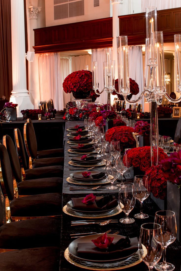 a long table is set with black and red plates, silverware, and flowers