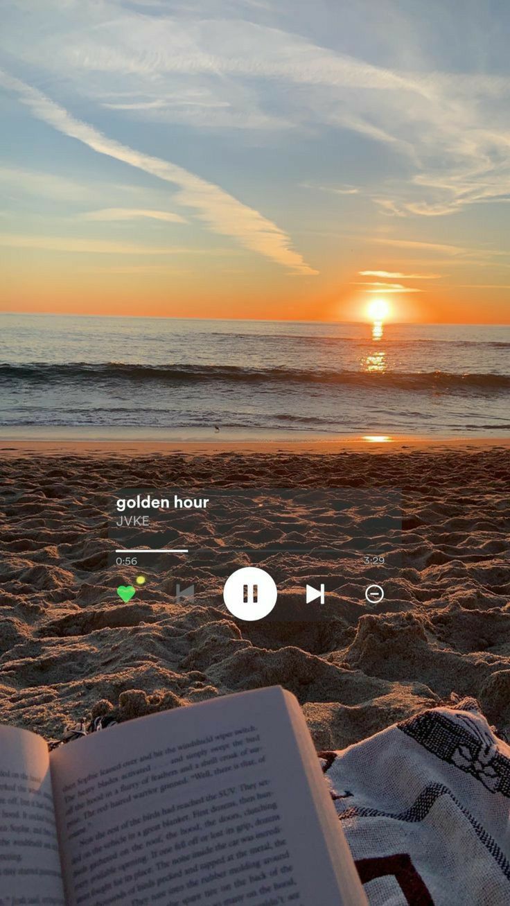 an open book sitting on top of a sandy beach next to the ocean at sunset