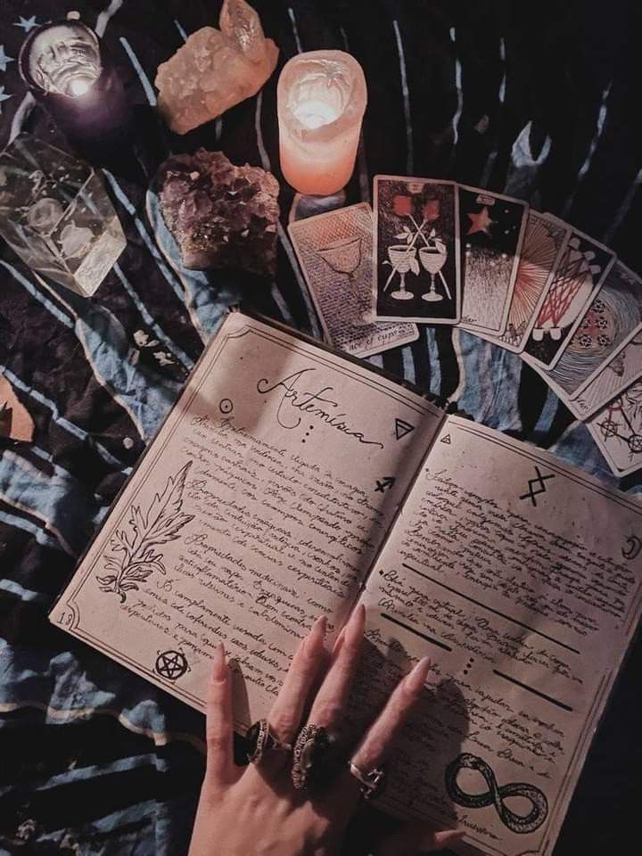 a person holding an open book surrounded by tarot cards and candles