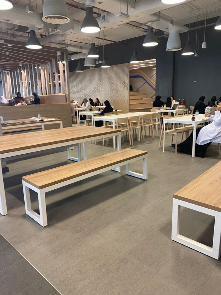 people are sitting at tables in an open area with wooden benches and white table tops