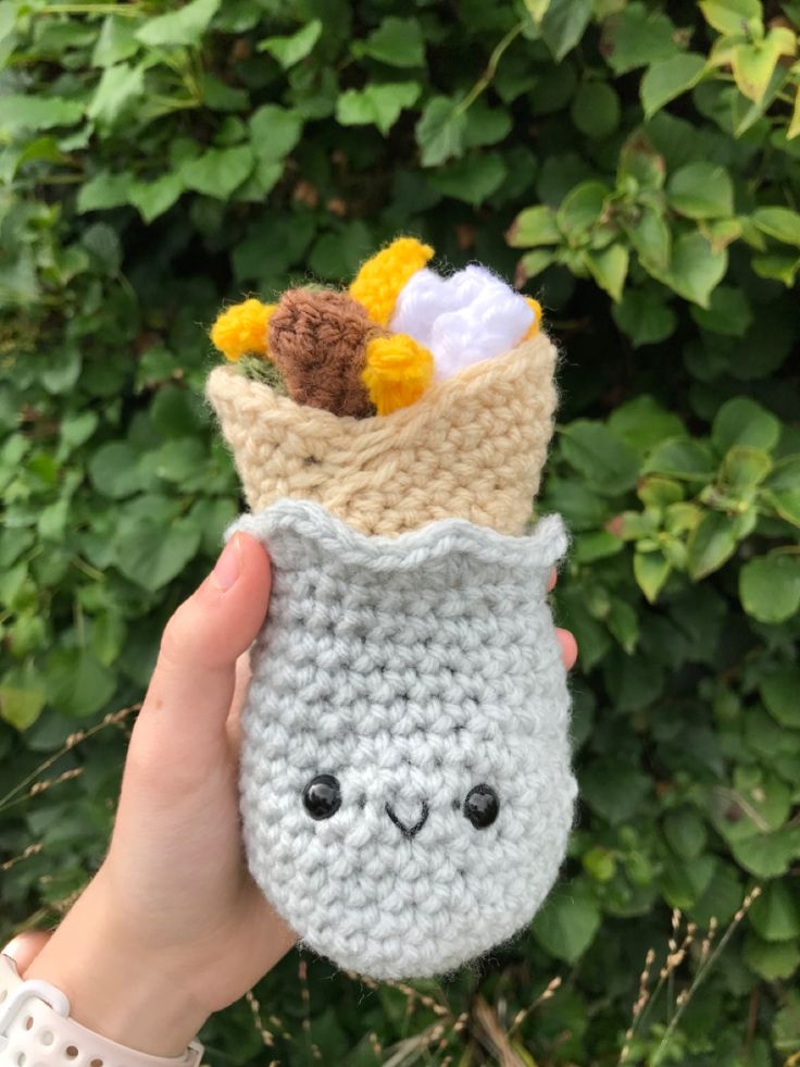 someone is holding up a crocheted cup with flowers in it and there is a stuffed animal inside