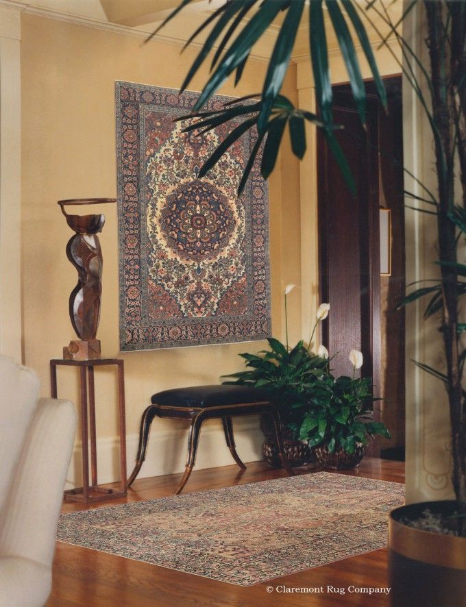 a living room with a rug on the wall and potted plant next to it