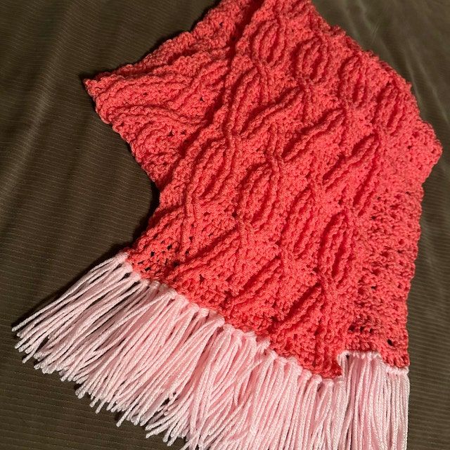 a red and pink blanket laying on top of a bed