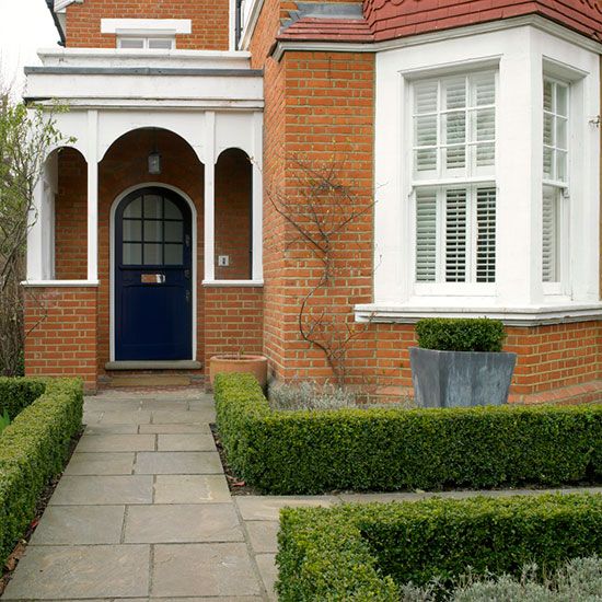 a blue door is in front of a brick house with trimmed hedges and bushes around it