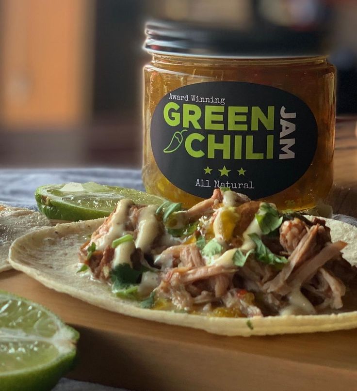 a tortilla topped with meat and salsa next to a jar of green chili mayo