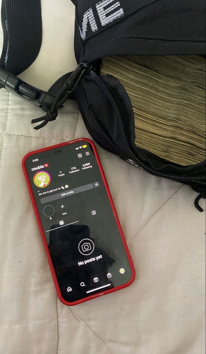 a red cell phone sitting on top of a bed next to a black bag and white sheets