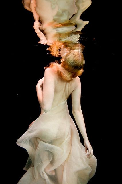 a woman in a white dress under water with her head above the water's surface